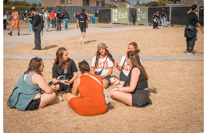 Groupe de bénévoles Basta assis en cercle sur l'herbe lors d'un festival, t-shirts "Basta" visibles