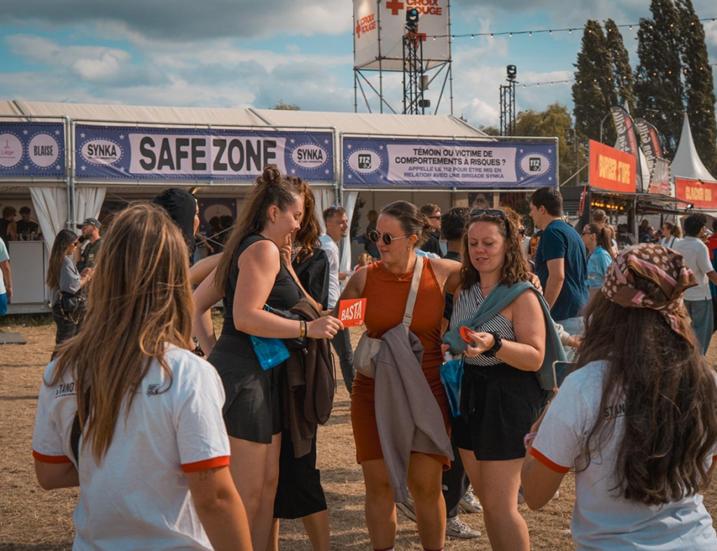 Bénévoles Basta distribuant des badges de sensibilisation à des festivalières devant le stand Safe Zone