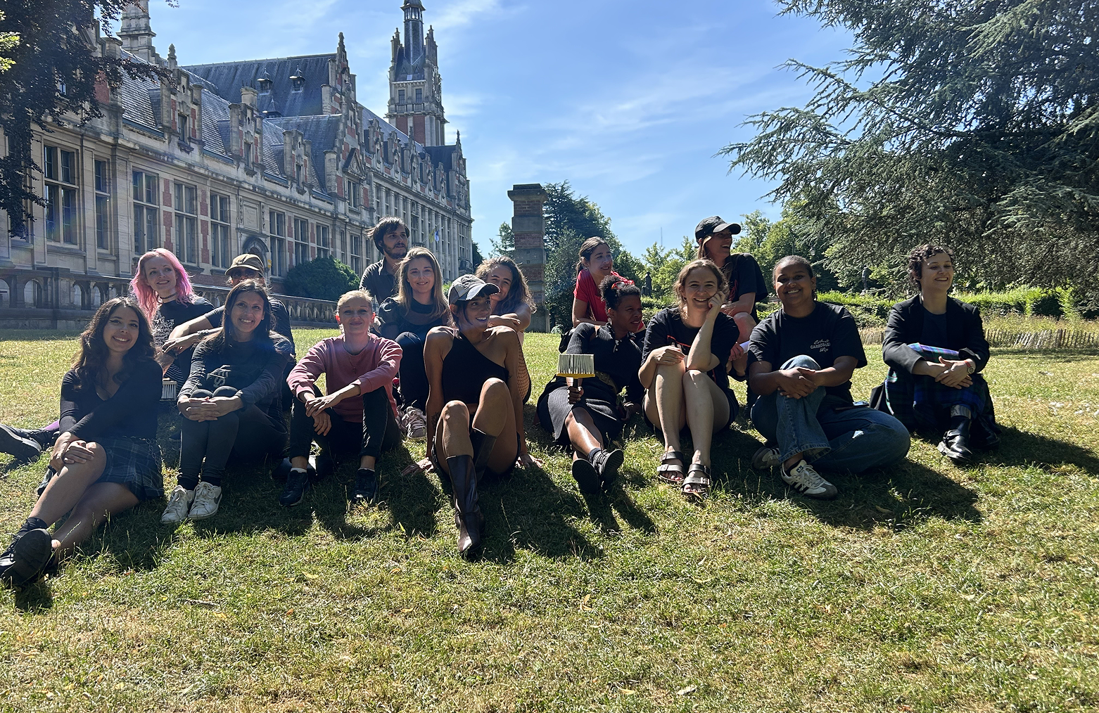 Équipe de Basta assise sur l'herbe devant un bâtiment historique bruxellois