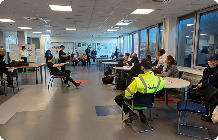 Session de formation Basta auprès d'employés, dont un agent en gilet fluo STIB, assis en cercle dans une salle