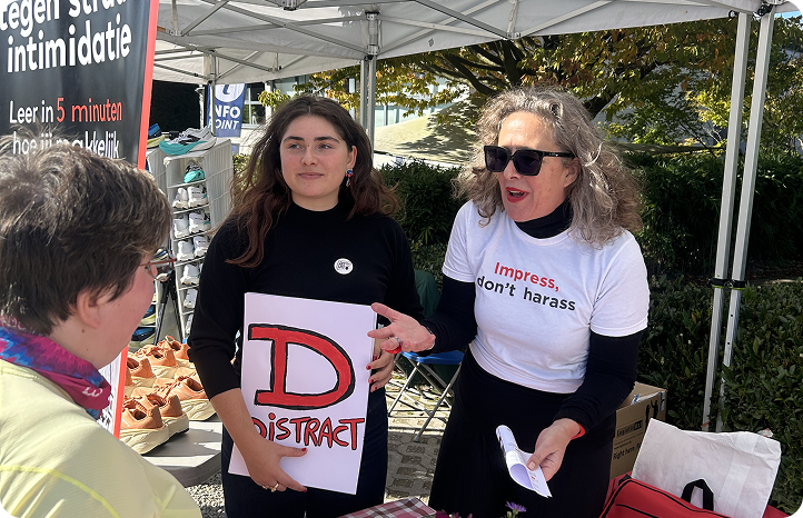 Bénévoles de Basta expliquant la méthode "Distract" contre le harcèlement de rue sur un stand, pancarte à la main