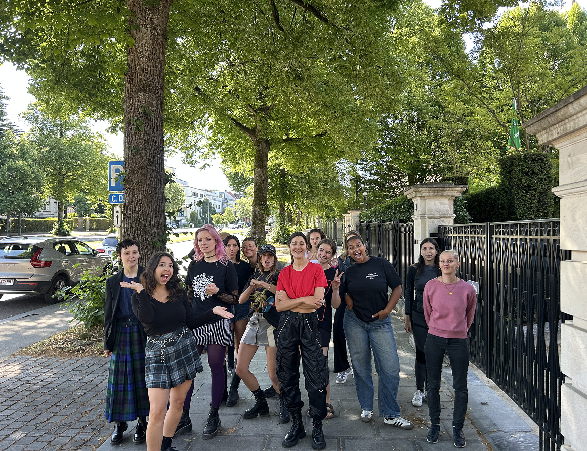 Photo de groupe de treize femmes souriantes posant dans une rue bordée d'arbres à Bruxelles